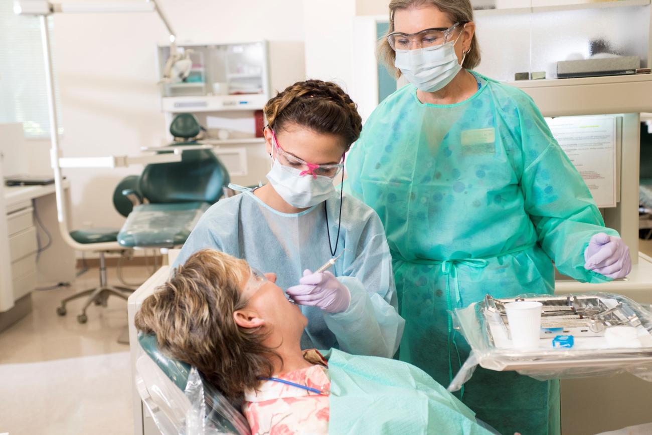A dental hygiene student next to a patient with a certified Dental Hygienist.