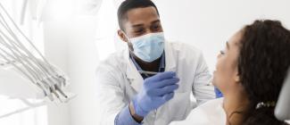 black male dentist wearing face mask works on black female in dental chair