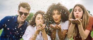 four diverse young people blowing confetti