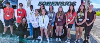 Eleven kids with an instructor standing in front of a Forensics truck.