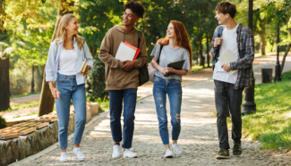 multiracial group of four students walking while talking and carrying books