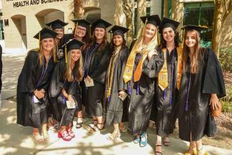 Nine PHSC women graduates posing together in their caps and gowns.