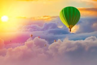 Scenery of a hot air balloon floating above the clouds as the sun shines.
