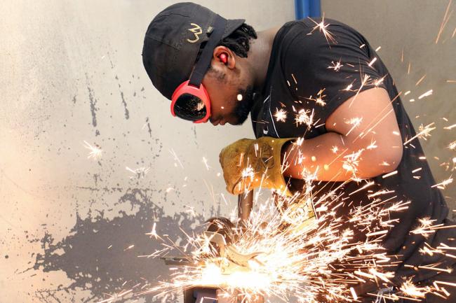 PHSC welding program student handling a saw machine as it produces sparks.