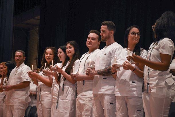 10 diverse nursing graduates wearing scrubs while holding a candle.