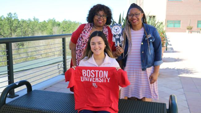 A PHSC student holding a Boston University t-shirt with two PHSC staff members