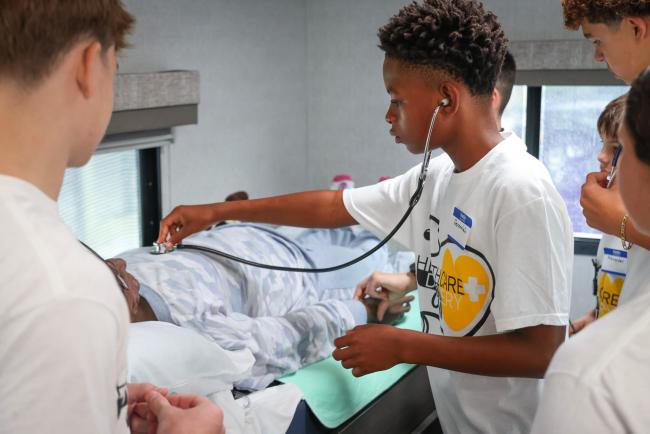 A camper using a stethoscope to listen to heart sounds on a mannequin in the Empath Health Mobile Simulation RV.