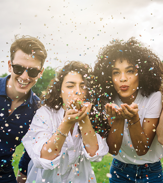 three young adults blowing confetti