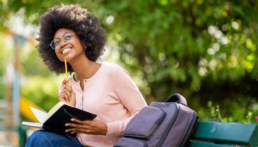 black girl with open book, backpack lying on bench
