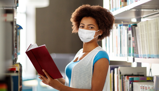 black female student wearing face mask and holding an open book